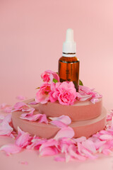 Rose essential oil in a glass bottle and rose flowers on a pink podium on a pink background.natural rose oil. Aromatherapy and cosmetics .Organic bio cosmetics