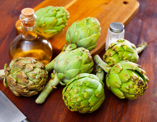 Obraz premium Organic green artichokes, bottle with olive oil and salt on wooden background, food preparation