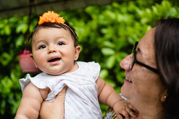 latina aunt with her baby girl niece smiling and playing outdoors - obrazy, fototapety, plakaty
