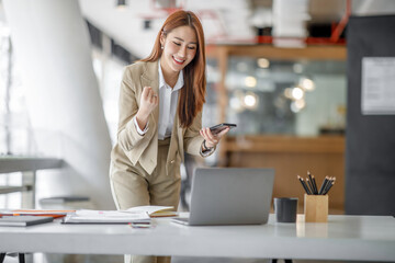 Happy excited successful Asian businesswoman triumphing in office