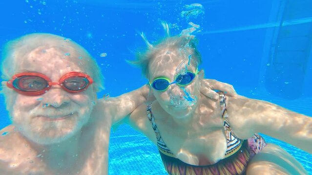 Couple of two happy seniors having fun and enjoying together in the swimming pool taking a selfie picture smiling and looking at the camera. Happy people enjoying summer outdoor in the water
