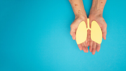 Lungs shape made from yellow paper on a palm old woman on a blue background - obrazy, fototapety, plakaty