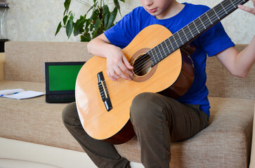 teenager boy playing guitar at home, online education lesson