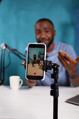 Veritical selective focus on live video podcast setup recording content creator moving hands gesturing. Closeup of smartphone filming influencer sitting down at desk with laptop smiling interacting