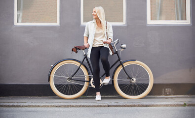 Fit and trendy. A beautiful young woman leaning on her bike on the side of the street.