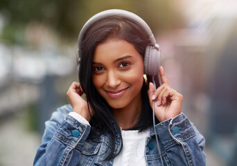 Music is what gets me going each day. Cropped shot of a young woman listening to music through her headphones while walking outdoors.