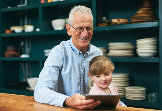 Spending Some Time With Grandad. Cropped Shot Of A Cheerful Elderly Man And His Little Grand Daughter Playing Around On A Digital Tablet Next To A Table At Home.