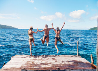 Let the summer madness begin. Rearview shot of a group of young women jumping off a pier and into...