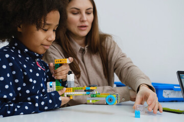 Multiethnic kids at STEM lesson constructing robot in classroom with woman teacher Children making electronic arm model at modern science school African American, Caucasian pupils learning technology
