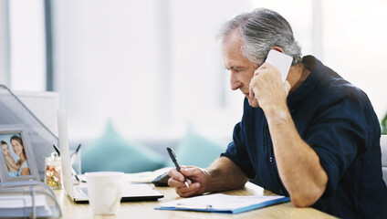 Handling business the best way he knows how. Shot of a mature businessman writing a few notes down while answering a phone call in his office.