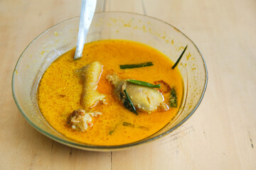 A bowl of (Opor Ayam) or chicken boiled in coconut milk is placed on a brown wooden table