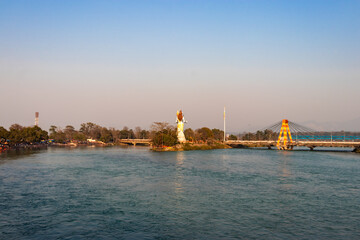 Naklejka premium hindu god shiva statue and isolated cable bridge over ganges river from back with bright blue sky