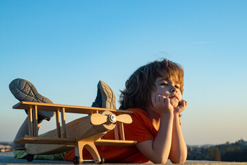 Kid 6 year old dreaming and plays with a toy plane in the park. Dreams of travel. Development, growth, dreams and plans. Imagination and dream concept.