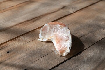 One slice of pomelo against a wooden background. Rough, cracked boards. Ready-to-eat food. Natural lighting.