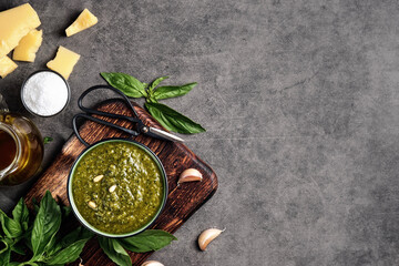Obraz na płótnie Canvas Italian green basil pesto in a gravy boat garnished with pine nuts. Ingredients for making pesto. Layout on gray kitchen table with copy space