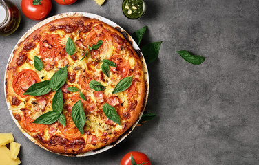 Homemade Italian pizza carbonara with ham and basil leaves on a dark background. Top view with copy space for text. Ingredients for pizza, cheese, butter and tomatoes on the table.