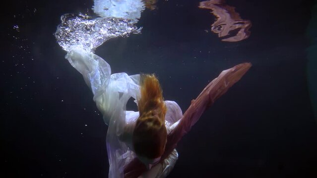 underwater view of a floating woman, graceful dance in a dress underwater as in a dream