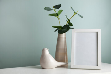 Cozy home desk table with vase with green branch, ceramic bird and photo frame.