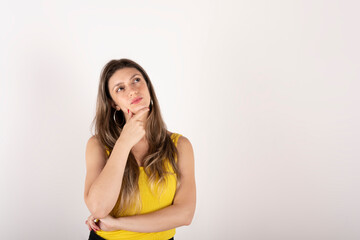 Fototapeta premium Portrait of a young blonde woman with a yellow shirt, on a white background, with a thoughtful expression, making a decision