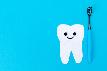 A plastic toothbrush and cartoon tooth cut out of felt on a blue background. Flat lay. Tooth and...