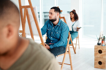 Naklejka premium Art is the last form of magic that exists. Cropped shot of a handsome young artist sitting and painting during an art class in the studio.