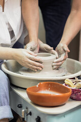 Hands close-up, men and women, a date in a pottery workshop, working together on one potter's wheel