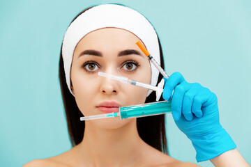 Portrait of a young attractive woman holding three syringes in hands near the face. Lught blue background. The concept of plastic surgery and rejuvenations injections