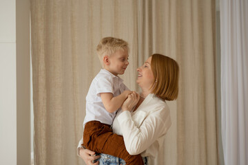 Mom and son with blond hair spend a good time hugging. Portrait of a family in the interior. Mother's Day. The relationship of children and their parents.