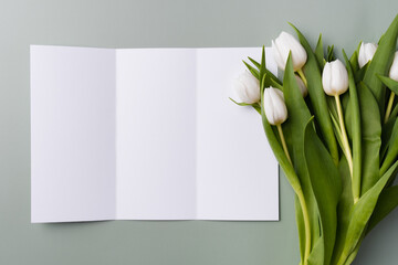 White mockup of trifold brochure on a pale green background with a bouquet of white beautiful tulips.