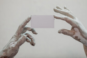 Hands in clay after work at the potter's wheel, close-up holding a mockup of a business card