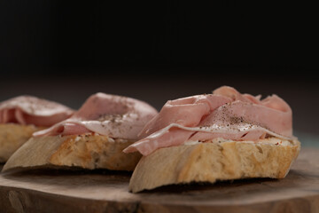 Toassted baguette slices with prosciutto cotto and cream cheese on olive wood board