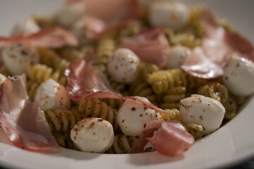 Pesto fusilli with mozzarella and coppa ham on white plate