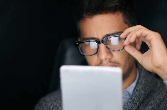 Whats The Latest On Social Media. Shot Of A Young Man Wearing Glasses Using A Digital Tablet In The Dark.