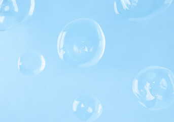 Several transparent drops of hyaluronic acid on a blue background, top view. Skin care and moisturizer.