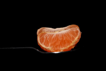 Two clementine slices on a spoon against black background