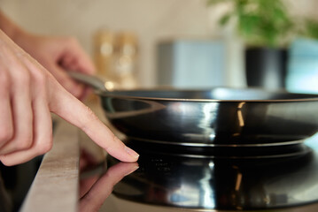 Modern kitchen appliance, Woman hand turn on induction stove with steel frying pan, Finger touching sensor button on induction or electrical hob
