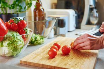 Woman cutting fresh cherry tomato for preparing salad in kitchen