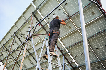 Male electrician wiring solar panels together. Man installing photovoltaic solar panel system outdoors. Concept of renewable energy sources.