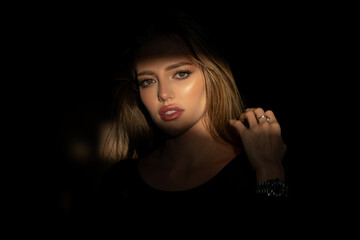 Elegant young woman posing over black background. Light and shadow. Portrait of a beauty woman face. Creative portraits with shadow and light over womans face, eyes on light.