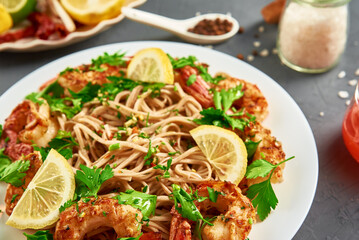 Stir fry noodle with shrimps, lemon and fresh parsley on white plate, soba with prawns, asian cuisine, top view