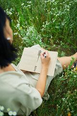 Female woman with pen writing or painting, handwriting on notebook on flower blooming meadow