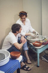 A couple in love in white shirts and jeans, a date in a pottery workshop, working together on one potter's wheel