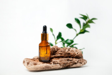 A glass brown bottle with facial serum standing on a piece of wood with a plant in the background. Copy space. The concept of organic natural cosmetics