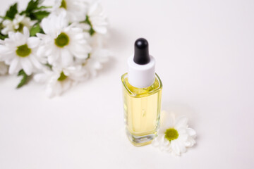 Top view on a glass bottle with essential oil and a chamomile flowers. White background. The concept of organic natural cosmetics