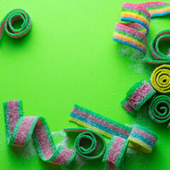 Rainbow stripes of sour jelly candies in sugar sprinkles on a green background with a place to copy. Top view. Colorful jelly candies in sugar sprinkles. Rainbow candy background. Selective focus