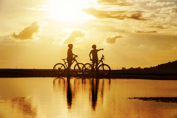 Fototapeta na wymiar Young Couple in love fun and happy riding mountain bike after covid-19 coronavirus outbreak. End of the coronavirus outbreak. Silhouette cycling man and woman riding mountain bike at sunset time.
