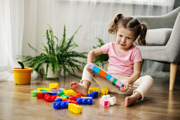 A little girl is sitting on the floor in the playroom and playing with colorful cubes, a constructor.