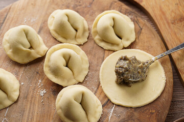 Process of preparation of traditional ukrainian east european dish varenyky - dumplings stuffed with potato-mushroom paste. Wooden background