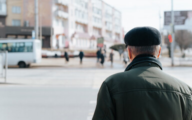 Rear view of senior man in cap and jacket standing on street, grandfather walking outdoors during day. Close-up, copy space