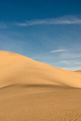 Fototapeta na wymiar Deserted landscape. Sand dune with dark shadow on a background of blue sky.